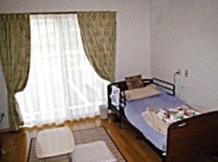 大きな窓のある、介護ベッドが置かれたワンルームの部屋
