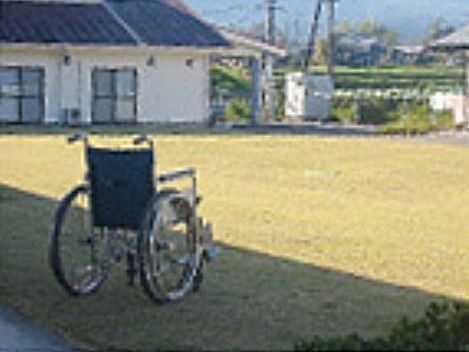 青い芝生が敷かれた中庭に置かれている、1台の車椅子
