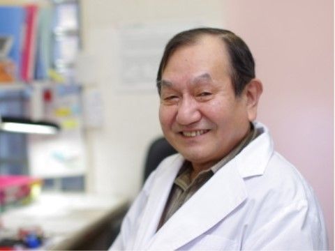 デスクに座って笑顔を浮かべている、白衣を身に着けた男性
