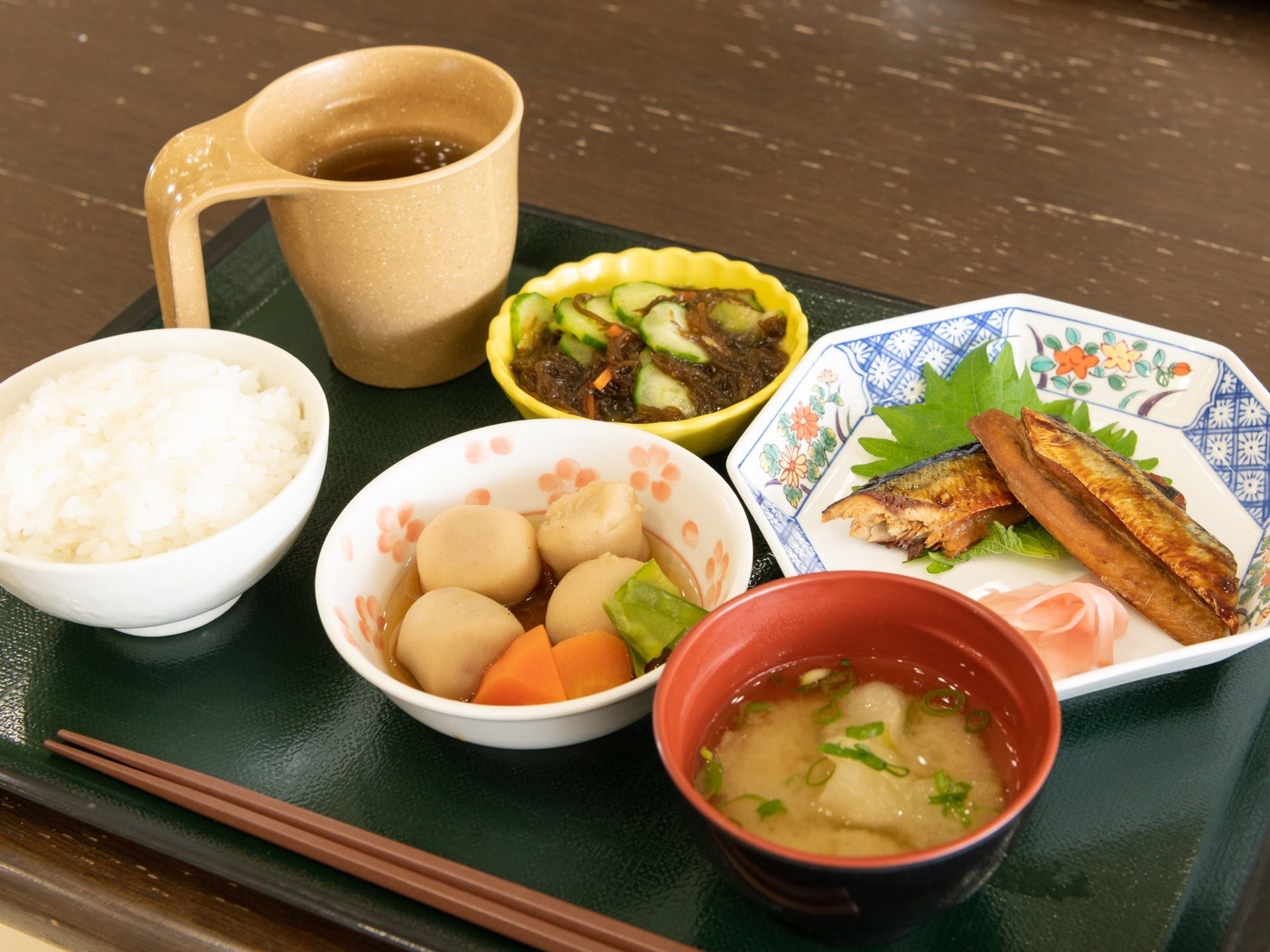 白米、味噌汁、里芋の煮物、モズクの酢の物、魚、そしてお茶が用意されている。色とりどりの食材を使っている。