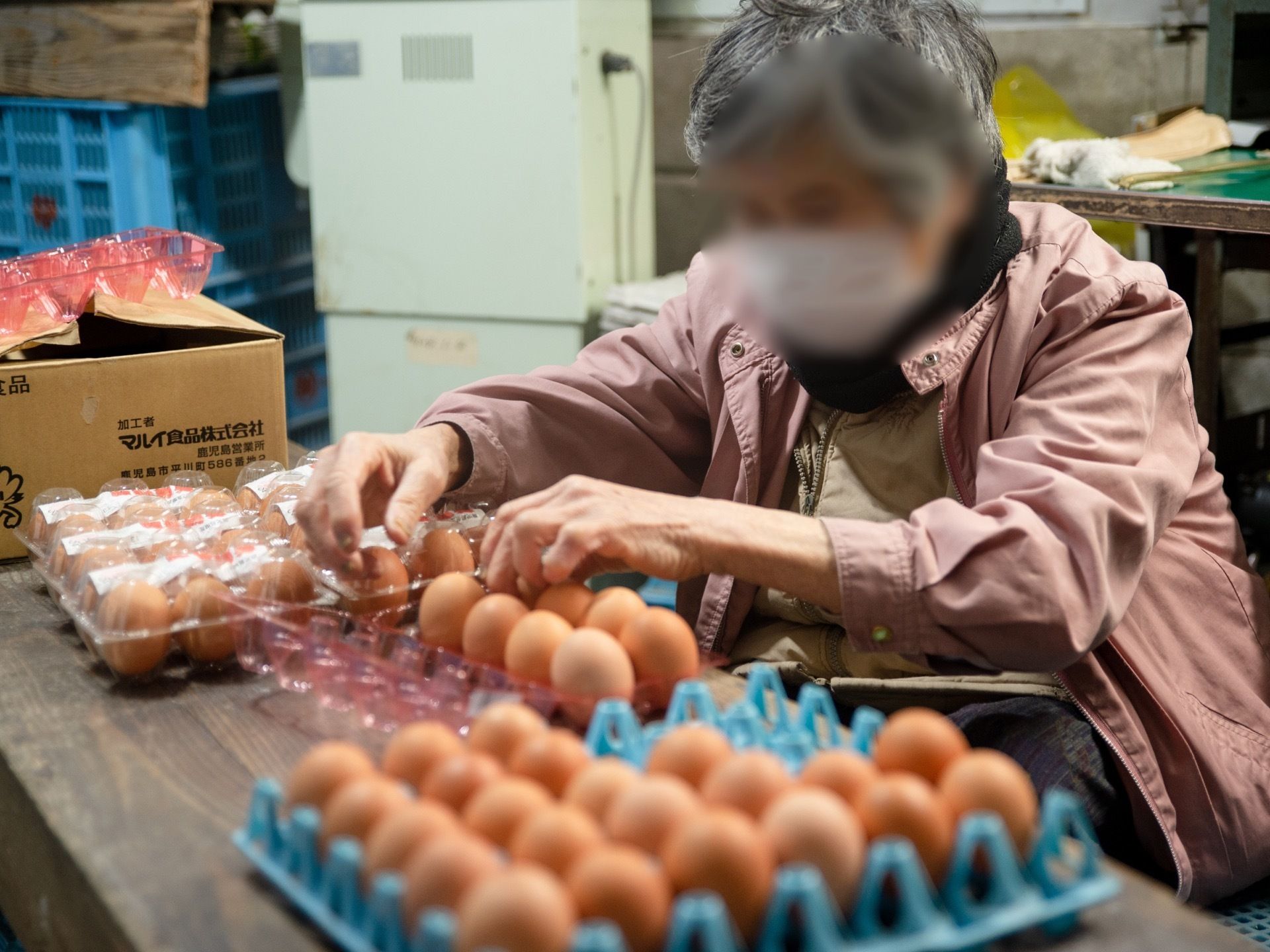 テーブルの上に卵がたくさん並べられ、入居者様が卵をパックに詰めている。卵はオレンジ色で、テーブルの端には箱が置かれている。