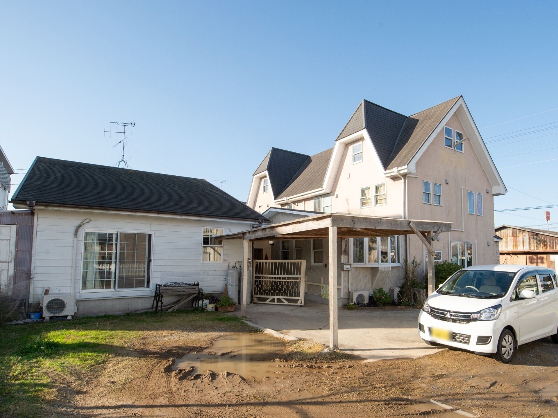 平屋と2階建ての2棟の建物があり、青い三角の屋根になっている。建物の間には白い門扉があり、側にはプロパンガスが置かれている。
