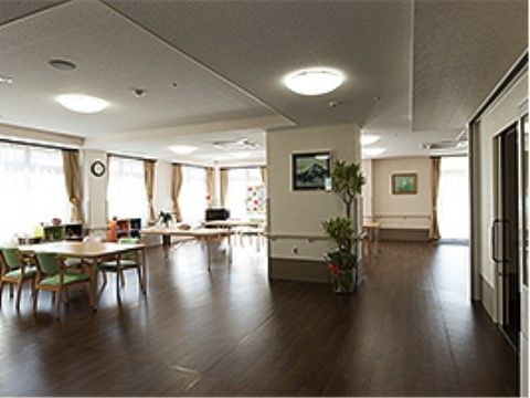 フローリング敷きの大きなホール。窓際にテーブルや椅子が置かれている。壁や中央の大きな柱には手すりが付いているほか、絵画も飾られている。