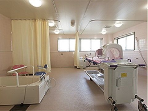 ベッドタイプの機械浴とストレッチャー、手すり付きの浴槽がある。床は物が置かれておらず整頓されている。奥にはカーテンで仕切られた空間もある。