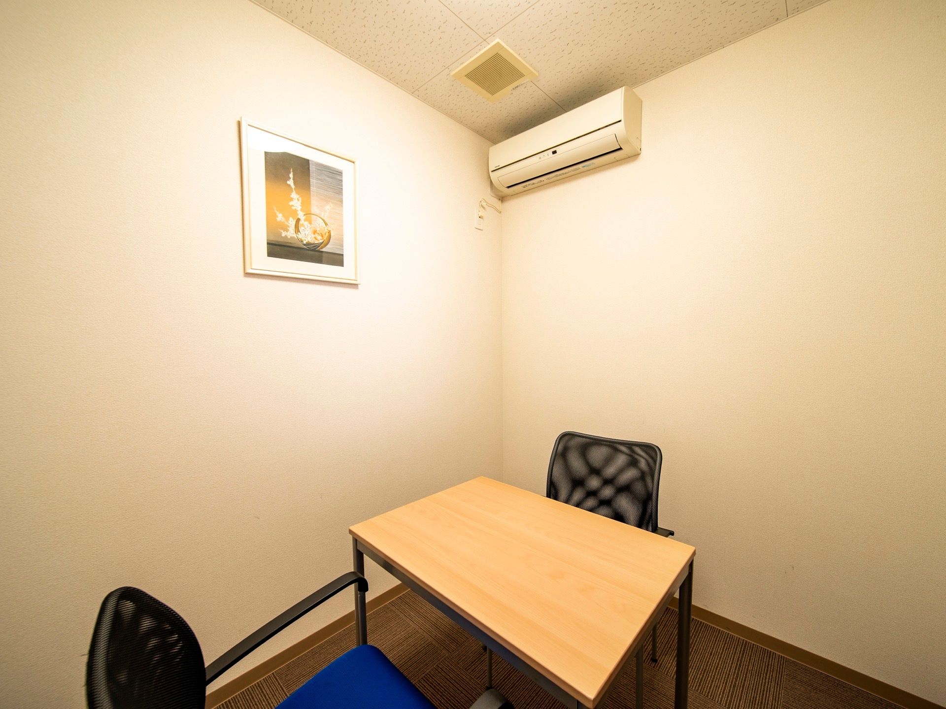四角い小さなテーブルと、椅子が２つ置かれた小部屋がある。壁には絵が掛けられており、エアコンが設置されている。
