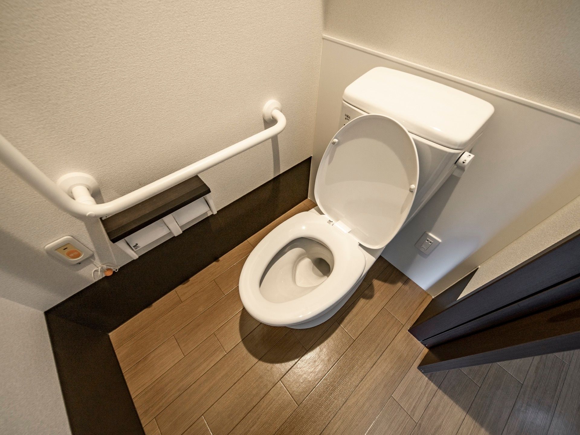 居室にあるトイレ。ドアはスライド式になっており、便器には蓋がある。壁には縦横方面に手すりが設置されている。
