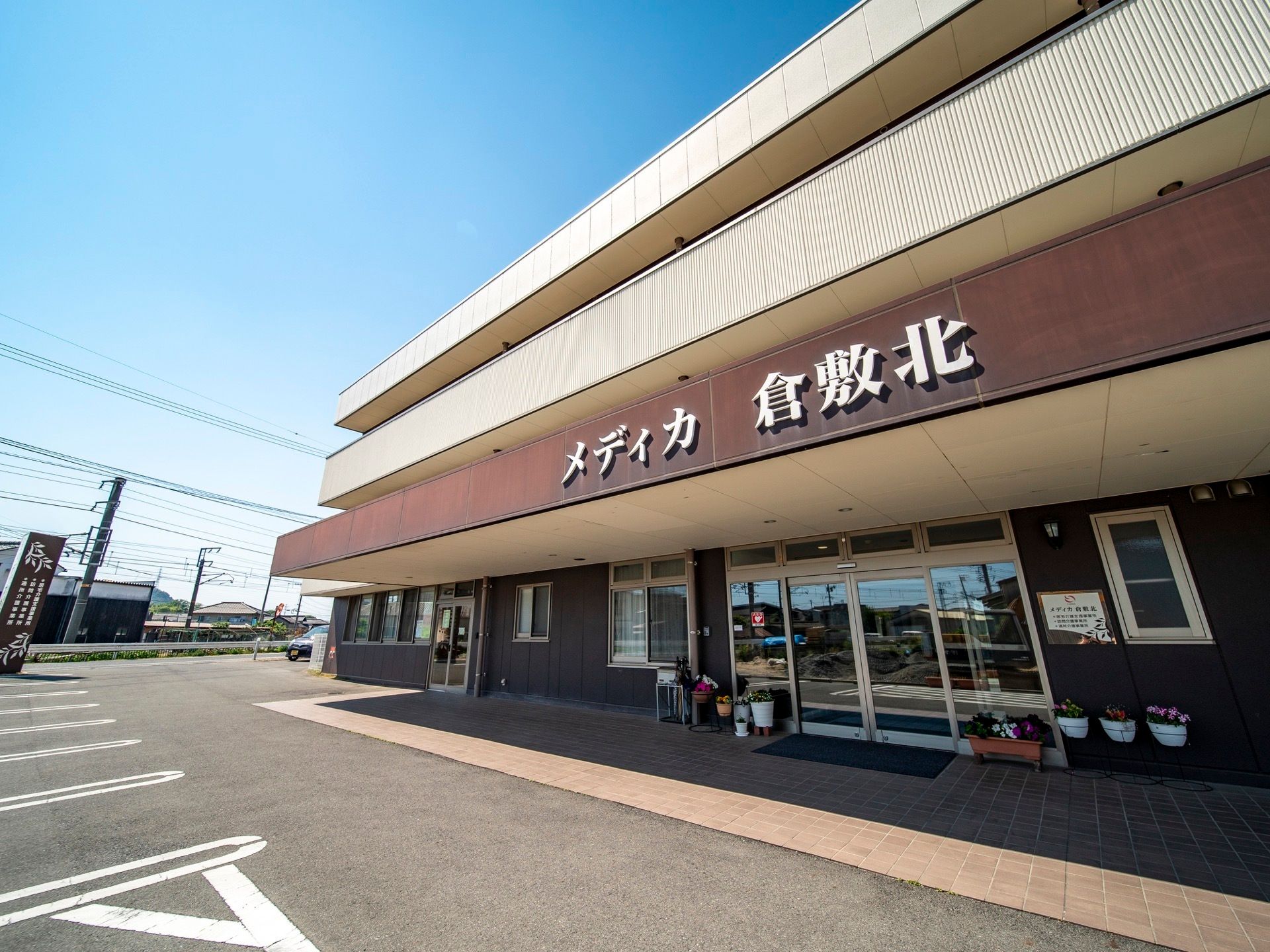 3階建ての大きな建物がある。1階部分は茶色、上部分は白い壁になっている。玄関正面の上には大きく施設名が書かれている。