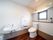 窓のついている広いトイレがある。室内には洗面台があり、側にはごみ箱が置かれている。背面の壁には棚があり、小物が用意されている。