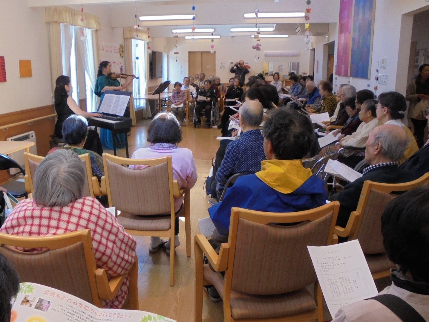 入居者様が音楽のイベントに参加されている。ピアノやバイオリンの演奏が響き渡る、広いイベント会場である。