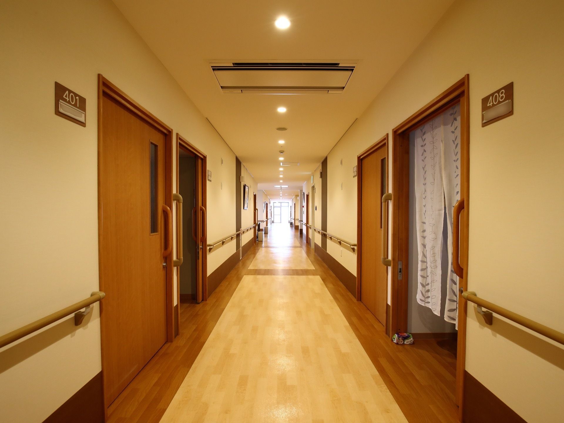 広々とした廊下の壁には歩行を補助する手すりが設置されている。左右に並ぶ居室の入口は大きな引き戸になっている。