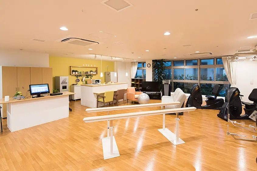 広い窓のある明るい室内に、歩行訓練用のポールや筋トレマシン、ストレッチボールなど、機能訓練用の器具が置かれている。