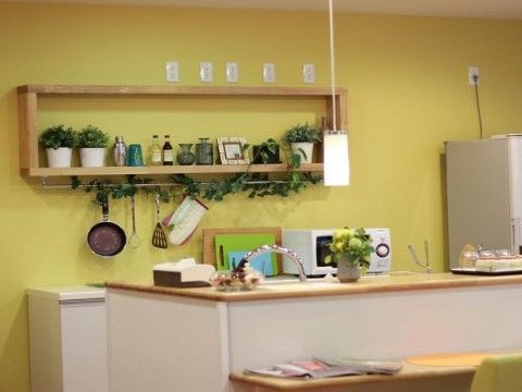 明るい黄緑の壁のウォールシェルフに飾られた瓶や植物などの飾りが可愛らしいオープンキッチン。スタッフは入居者様の様子を見ながら作業ができる。