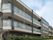 ブラウンとベージュの外壁で、ベランダがついたマンションタイプの建物である。施設の周りには植木が植えられている。