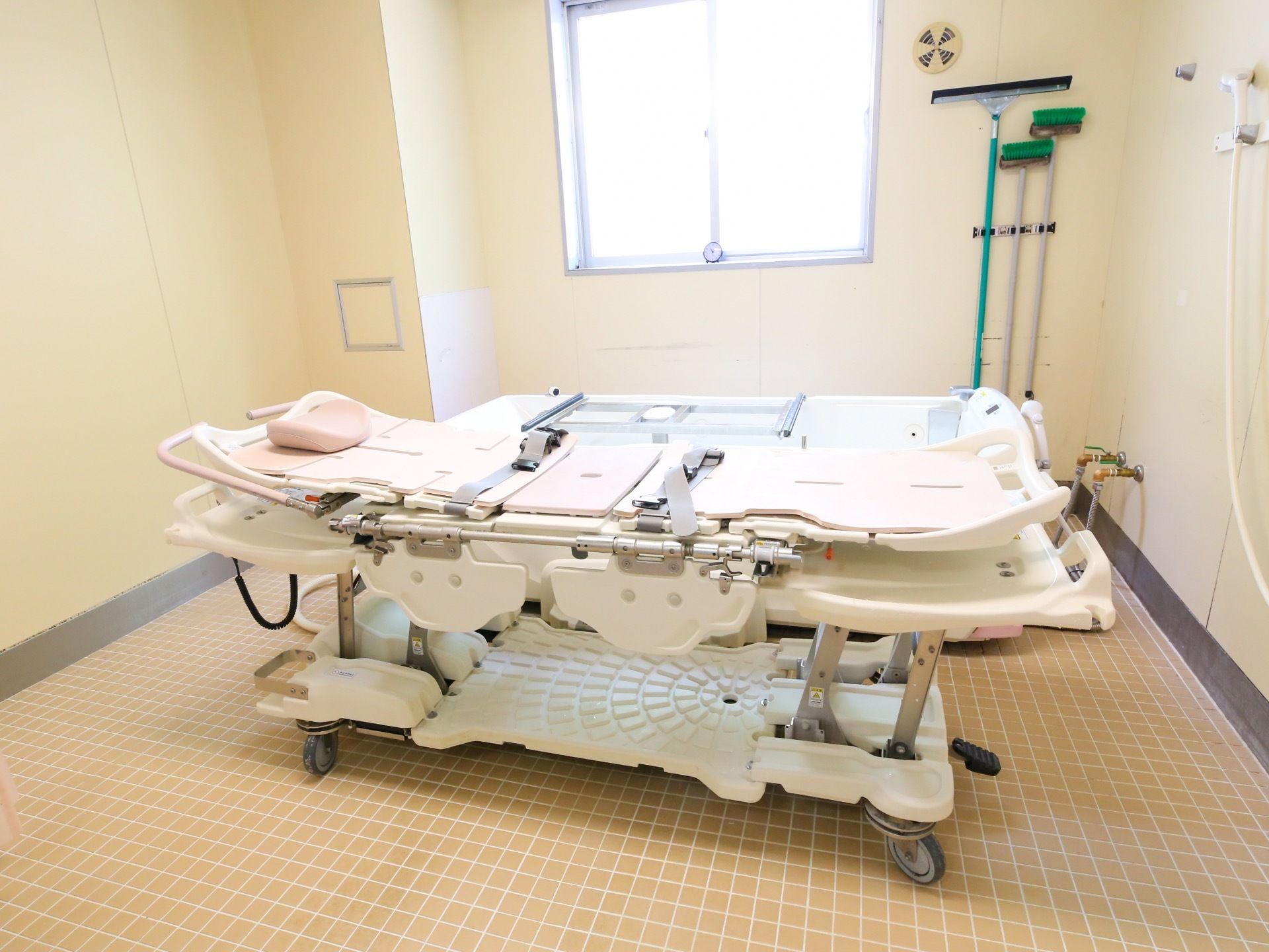 窓が付いた浴室に介護用特殊入浴装置が据えられている。窓側に浴槽が置かれており、手前に車輪が付いたストレッチャーが置いてある。