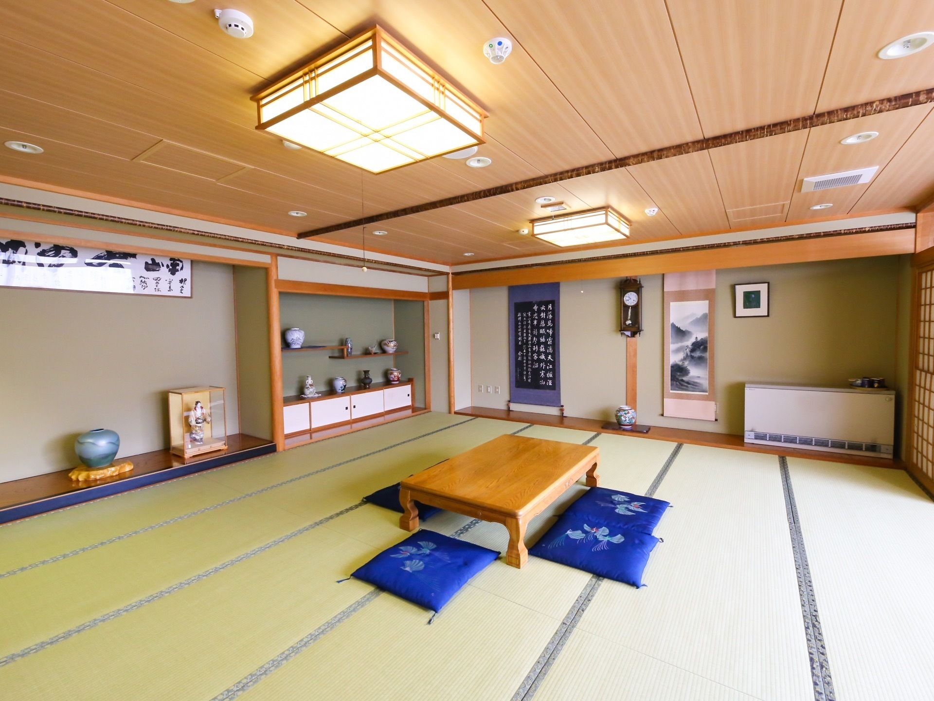 広々とした和室の中央に、木製の座卓と座布団が置かれている。周囲の壁には、書や美術品などが飾ってある。