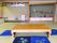 畳の部屋に、木製の座卓と青い座布団が置かれている。床の間や飾り棚には、壺や人形、額装された書などが飾られている。