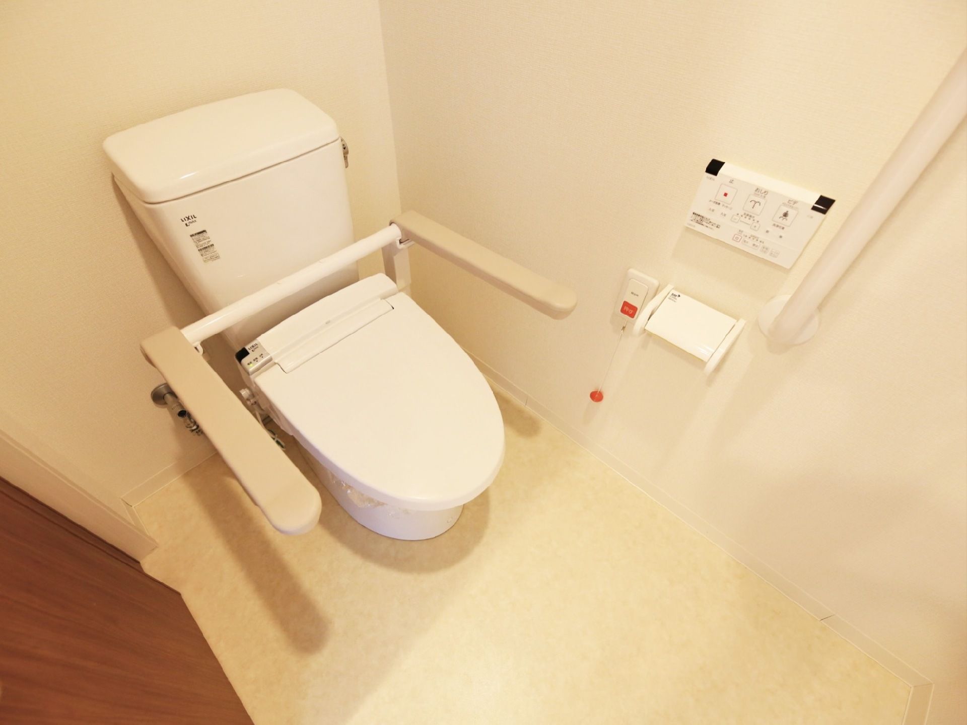 トイレは白で統一された清潔感溢れる空間である。トイレの便座には上方へ折りたたむことができる手すりが備わっている。