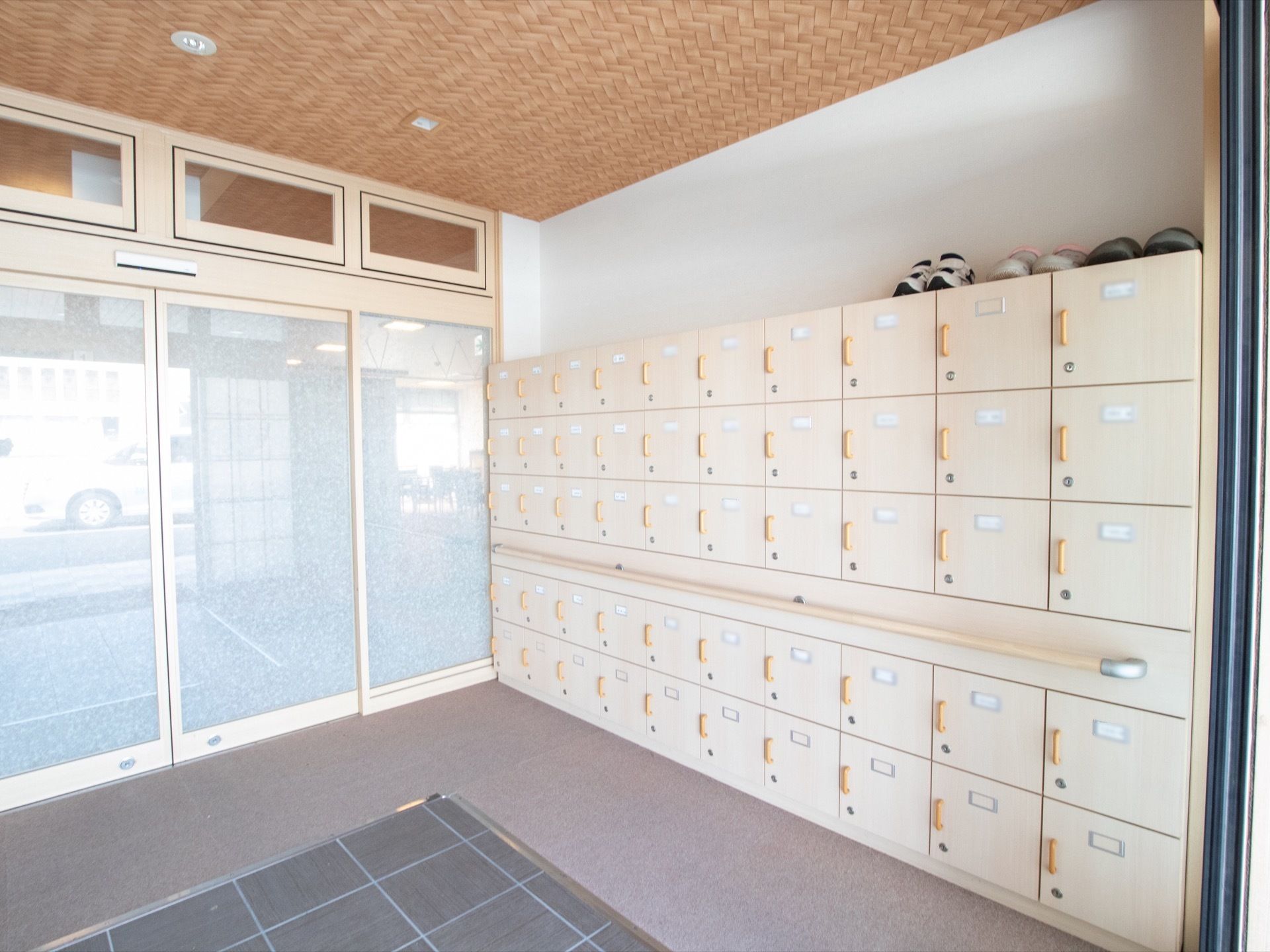 手すりの付いた大きな下駄箱が置いてあり、その上に靴が３足並んでいる。出入口はすりガラスでできた自動ドアである。