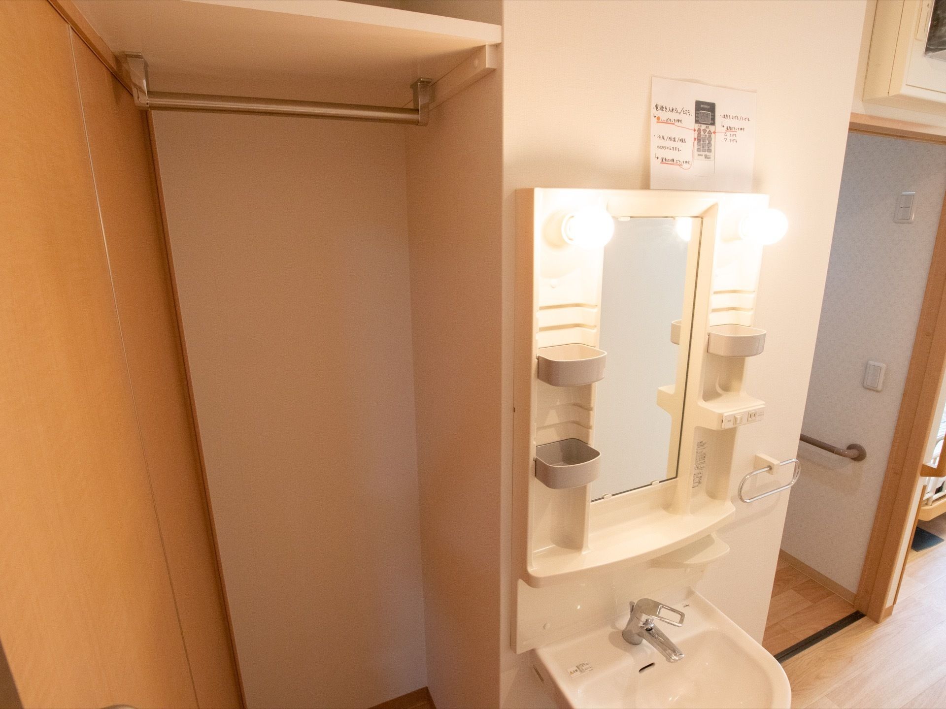 洗面台には、電球が付いており歯ブラシなどを置くトレーが複数ある。左隣には、ハンガーバーが付いたクローゼットもある。