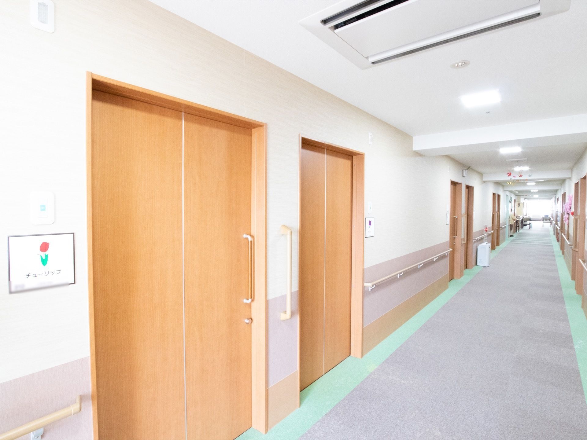 廊下の床や壁には、落ち着いたカラーを数色用いている。スライド式のドアに取っ手があり、また壁にも縦向きの手すりが設置してある。