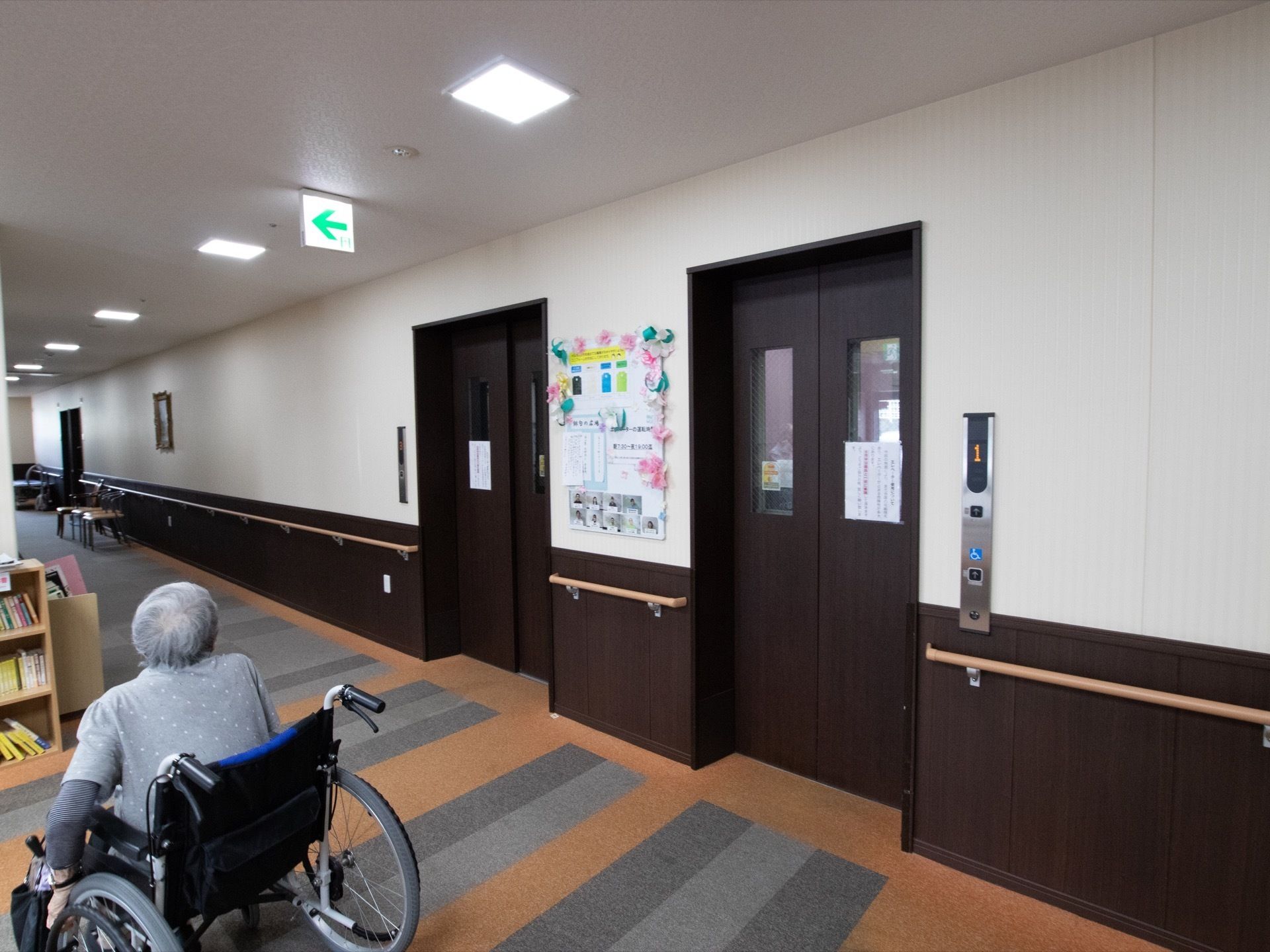 廊下の手すりから足元側は、濃い茶色の板を設置している。また同系色のドアのエレベーターがあり、車椅子をご利用の方も移動しやすい。