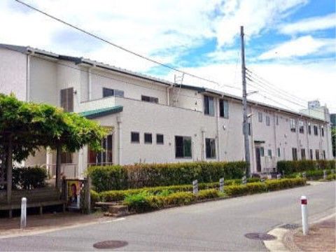 植木が植えられた緑の豊富な通りに面して建てられた２階建ての建物。壁の色は明るく、シンプルなデザインである。