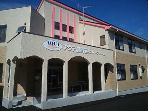 エントランスはスロープとなっているので、車椅子も楽に出入りが行える。ベージュの外壁に施設名とロゴが掲げられている。