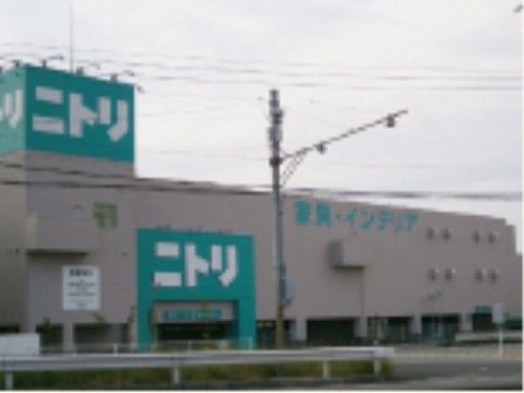 ベージュの壁の長方形のコンクリートの大きな建物。グリーンに白文字でニトリと書かれた大型看板が、屋上と駐車場出入り口の壁面に掲げられている。
