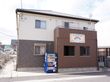 施設は道路に面して立っている。二階建てで階ごとに塗り分けられ、施設名の入ったベランダが増設のようになっている。