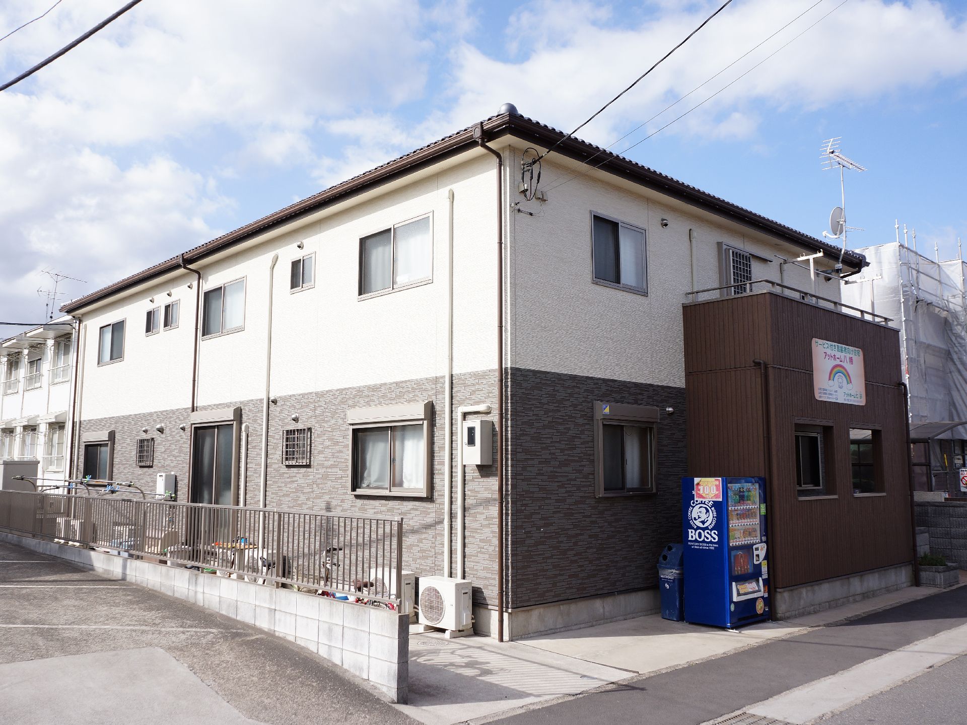 1階部分がグレー、2階部分がホワイトのアパートのような建物。道路に面した部分のベランダに施設名が入っている。