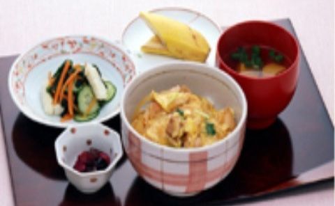 親子丼やお吸い物、漬物やバナナが並べられた黒いトレー