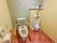 共有トイレには、男性用便器と介護用便座が並んで設置されている。便器の上には棚があり、消毒用スプレーや洗浄スプレーなどが置いてある。