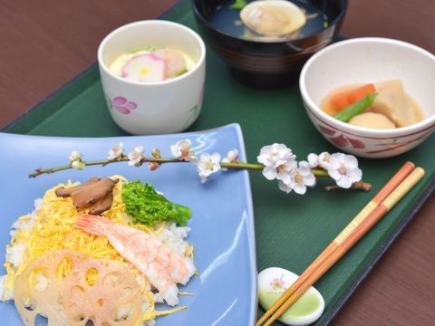ちらし寿司、茶わん蒸し、野菜の煮物、アサリのお吸い物にサクラの花が添えられている。箸置きにもサクラが描かれている。