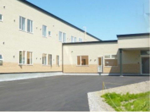 建物は２階建てで、玄関には屋根が付けられている。壁の色は明るいベージュ系で統一されており、窓が多くみられる。