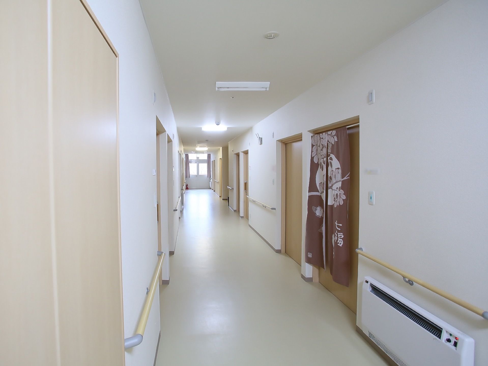 長い通路の奥に窓が設置されている。通路の両側にたくさんの扉があり、のれんが掛かった扉もある。手すりの下に暖房器具が取りつけられている。