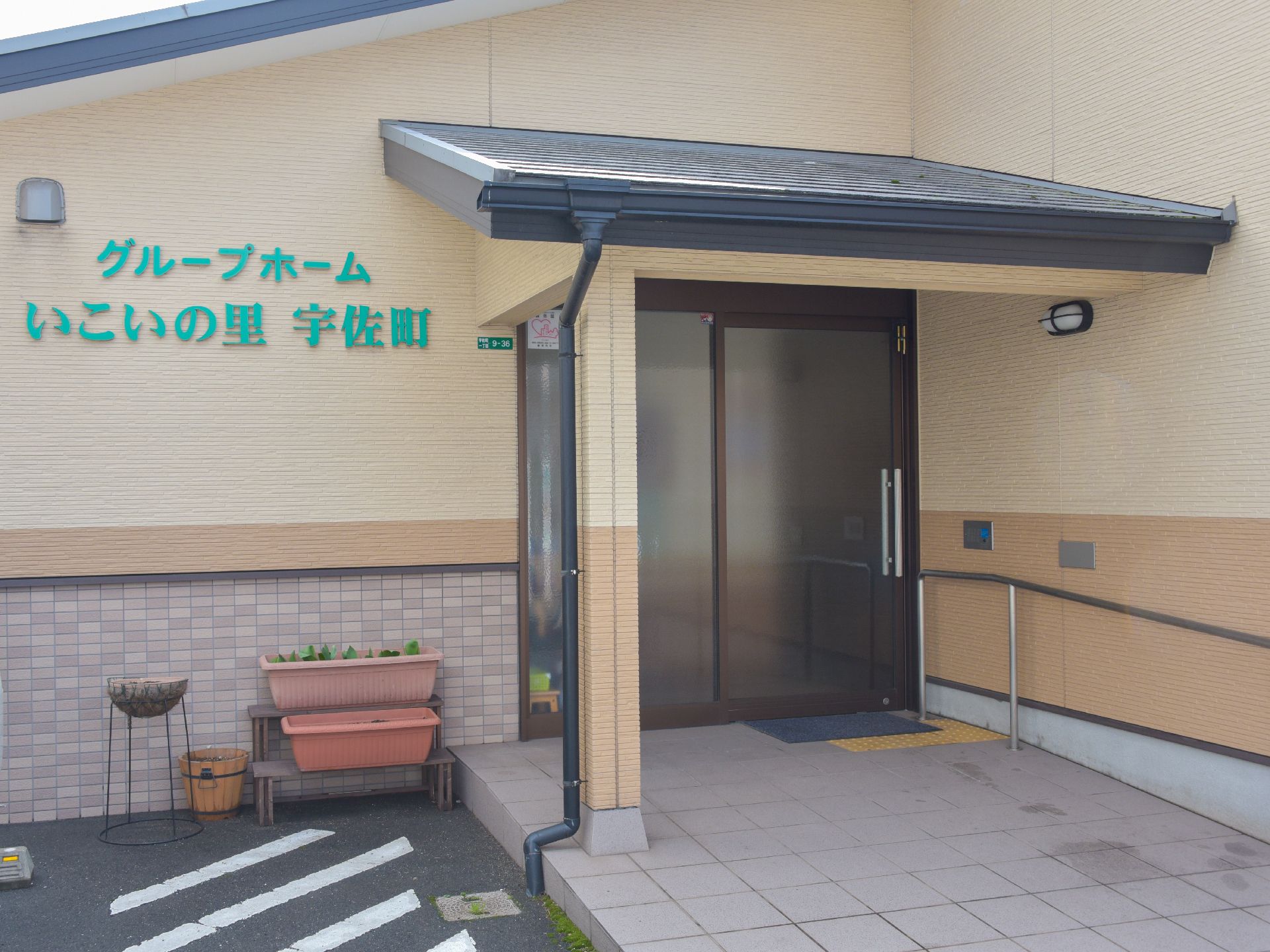 施設の正面玄関には大きく施設名が書かれており、すぐ横は車の駐車スペースとなっている。緩やかなスロープに手すりもある。