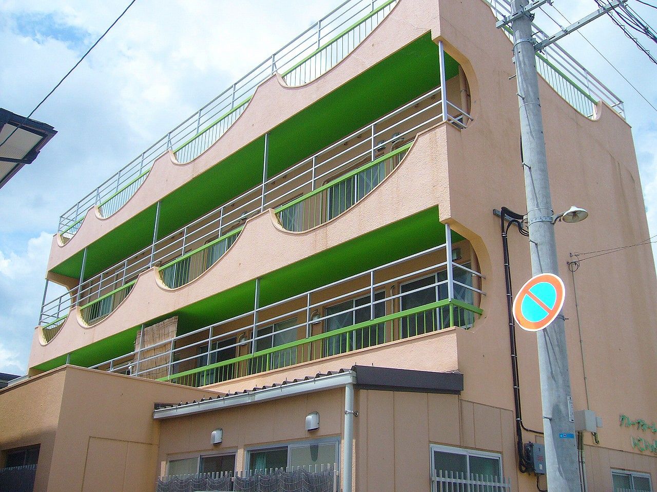 大学に近い住宅街にある集合住宅型のホームである。暖色系の壁にベランダの緑色がデザイン性のある、モダンな外観である。