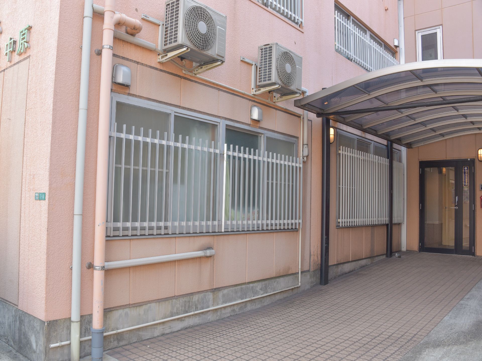 施設入口付近に窓がずらりと並んでいて柵格子で防犯対策をしている。また入口には大きな屋根が取り付けられている。