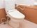 白色と茶色で統一された落ち着く空間のトイレには転倒防止になる白くてまっすぐな手すりが取り付けている。
