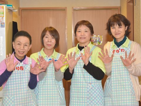両手を広げて笑顔で写る、エプロンを着た４人の女性スタッフ