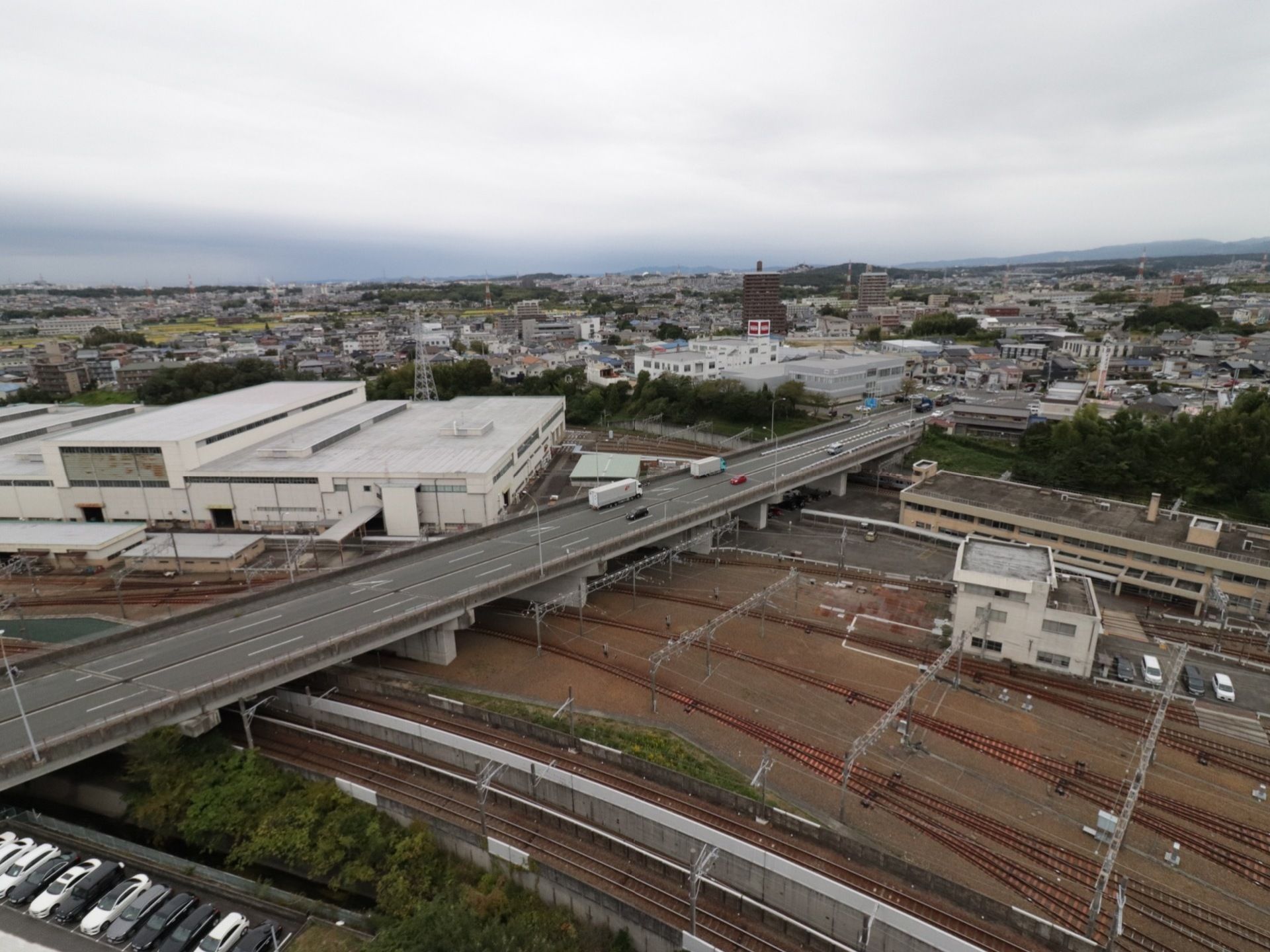 居室のベランダから眺めた風景。街並みと緑がバランスよく融合した日進市の様子が見える。近くには自動車合道と鉄道路線がある。