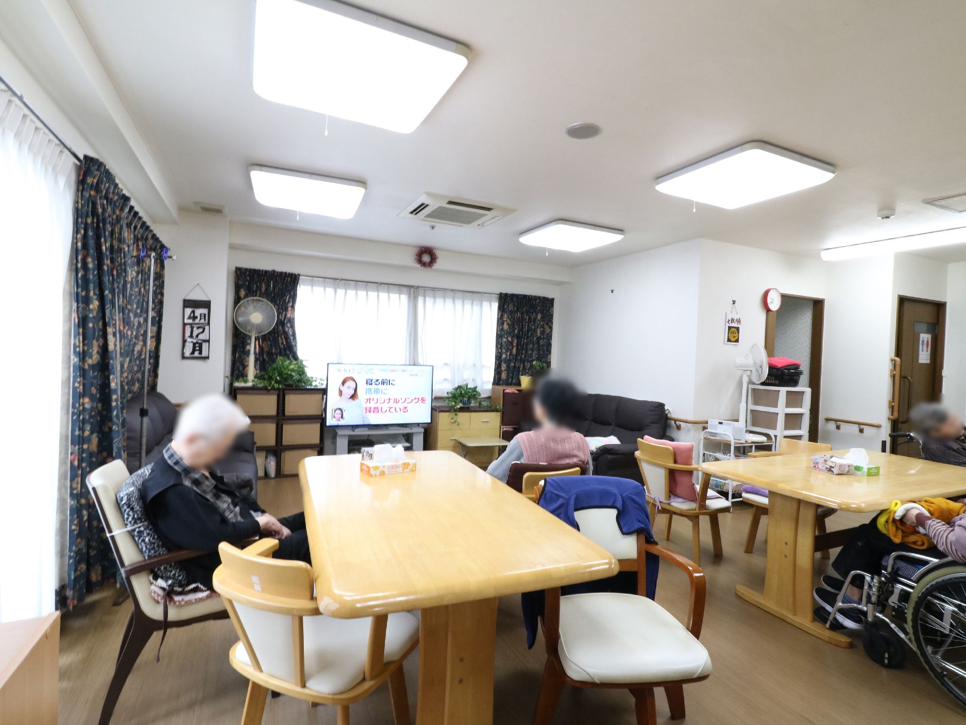 テーブルや椅子が並べられた部屋である。施設利用者が集まってテレビを見る等してくつろぐ。また壁には手すりが設置されている。