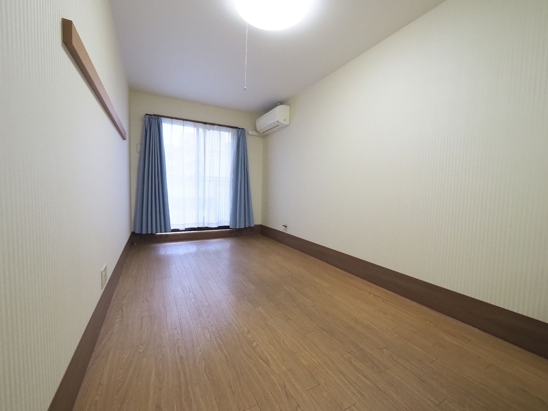 入居者用の個室にはレースのカーテンと青いカーテンが窓際にかかっている。エアコンも取り付けられている。