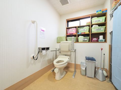 トイレは広くて、手すりが設置されている、トイレの後ろ側の棚には入居者の部屋番号が書かれた入れ物にそれぞれのタオルが入れられている。