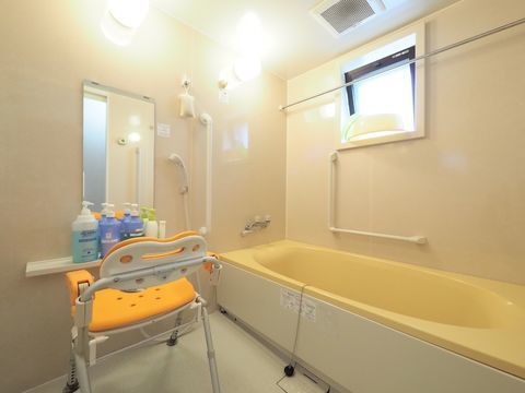 お風呂にはL字型と縦型の手すりが取り付けられている。黄色い介護用お風呂椅子も置かれている。浴槽も黄色い。