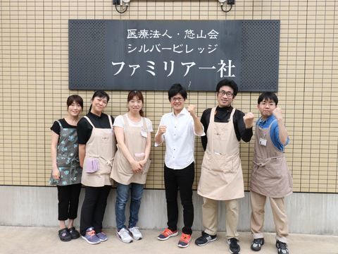 施設名が書かれた看板前で写真撮影する６人のスタッフ