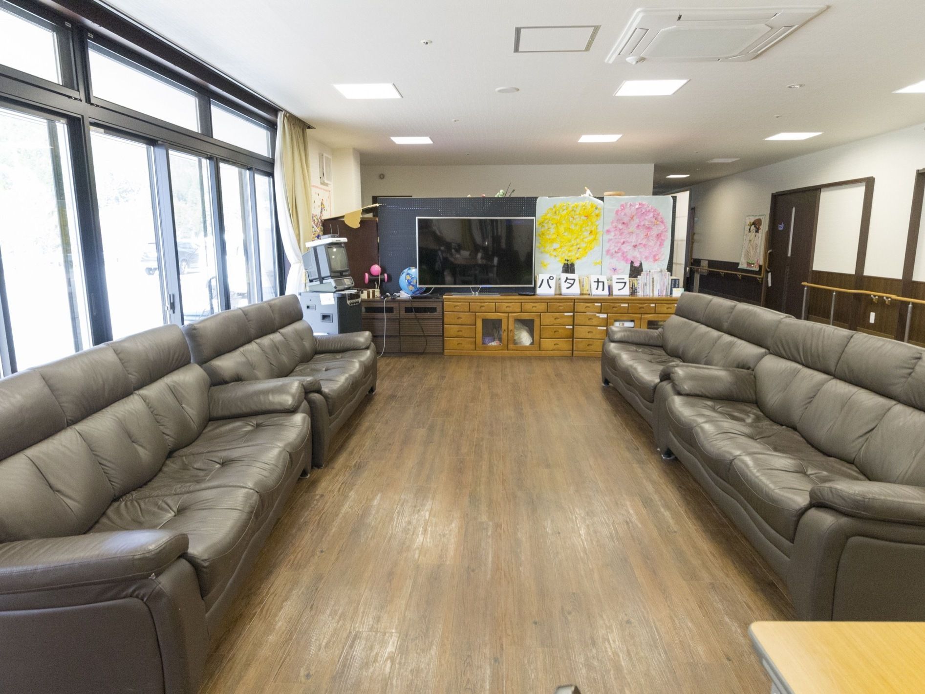 明るい談話室の両側には灰色のソファーが奥まで配置されており、入居者様は多人数で休憩や談笑をすることが可能である。