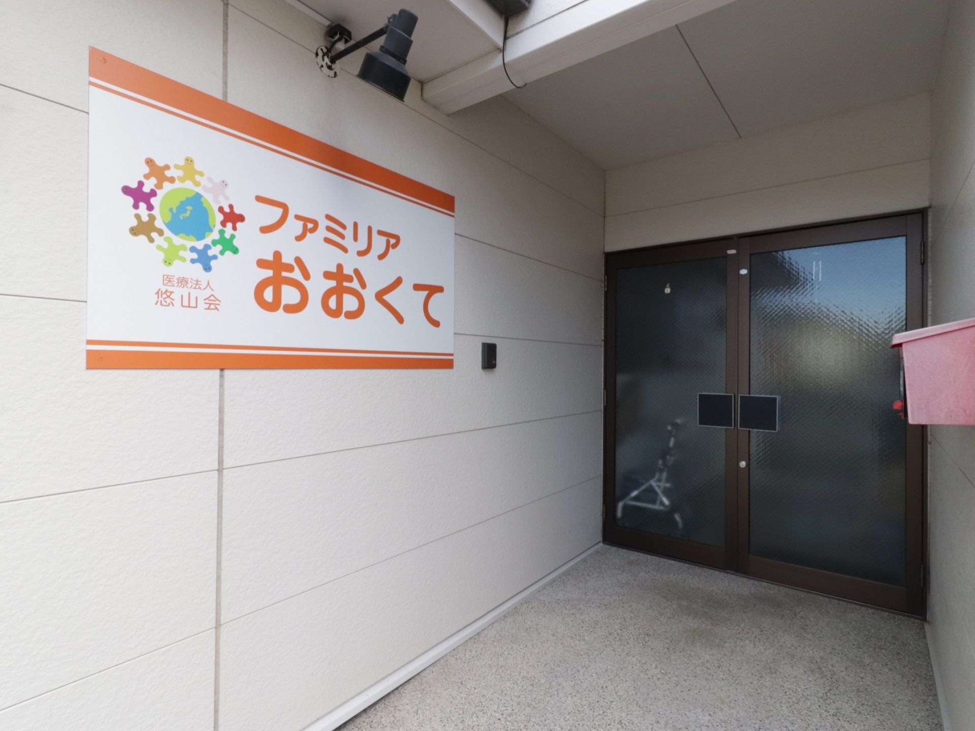 玄関の扉は手前に引く形になっている。ブラウンの縁取りがされており、落ち着いた雰囲気である。施設名がオレンジ色で書かれていてわかりやすい。