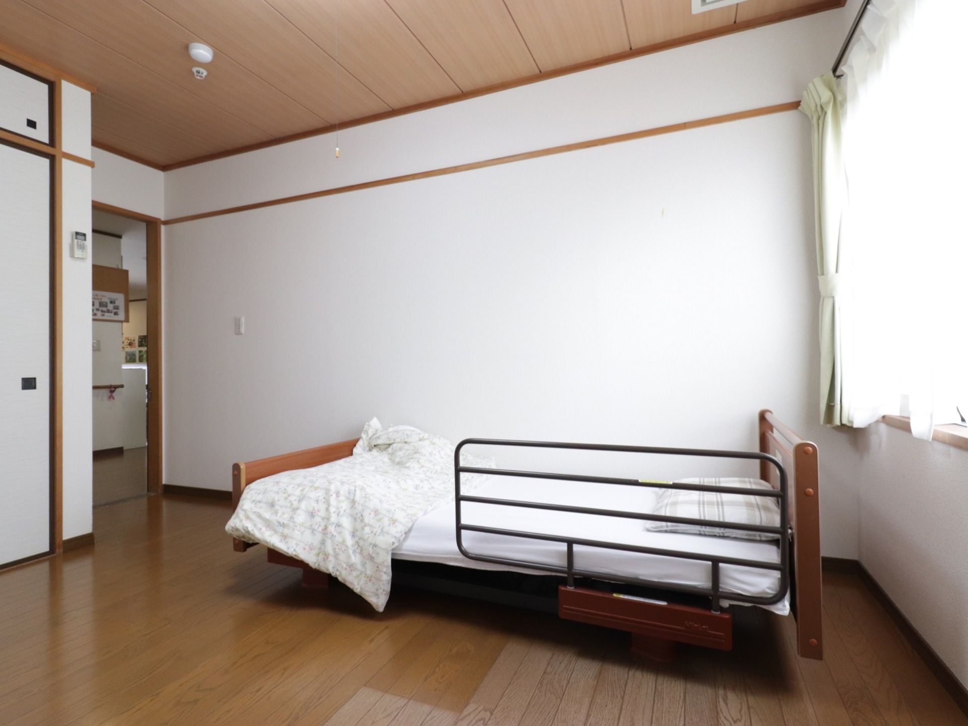 白い壁と大きな窓がある明るい居室になっている。天井と床は木目になっており落ち着いた雰囲気になっている。