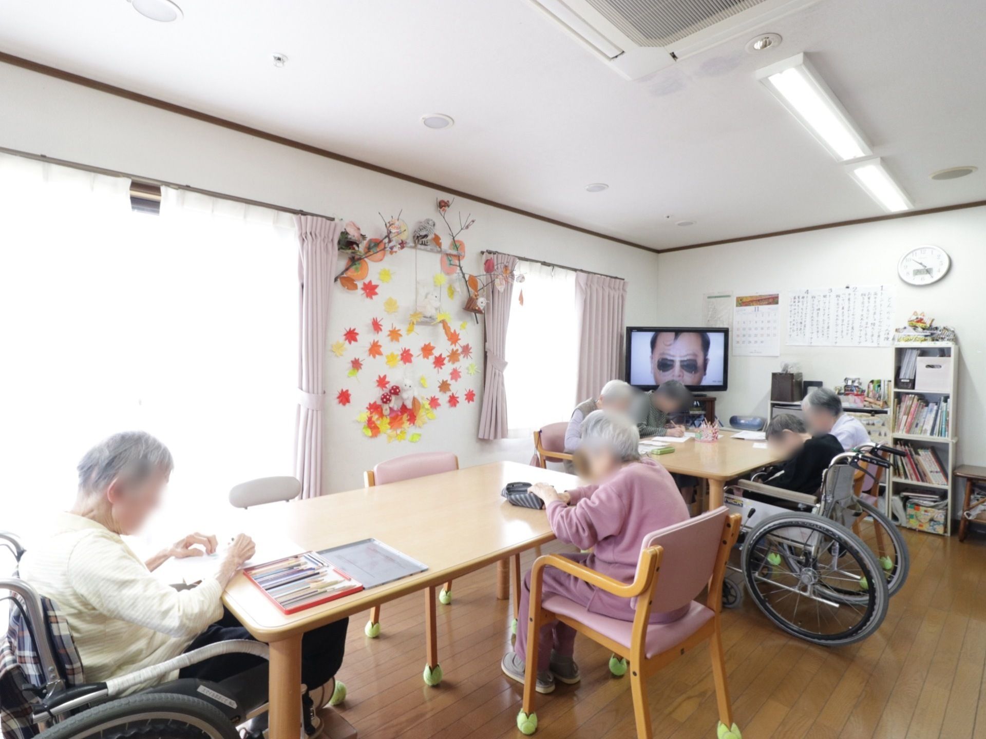 窓から光が差し込む明るい休憩スペースで、塗り絵などをしている入居者様たち